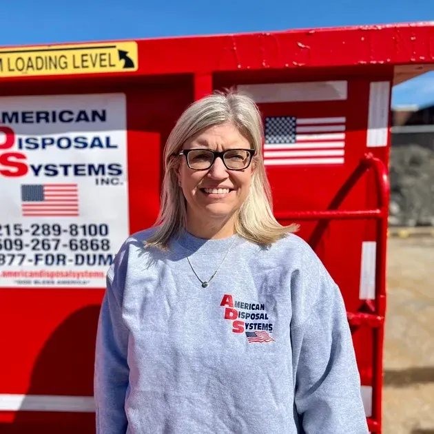 Becky Kasper Shemeley standing in front of a red roll off trash container