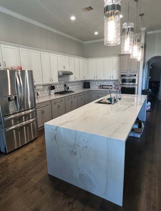 Modern kitchen with white and gray cabinets, large island, stainless steel appliances, and dark wood floors.