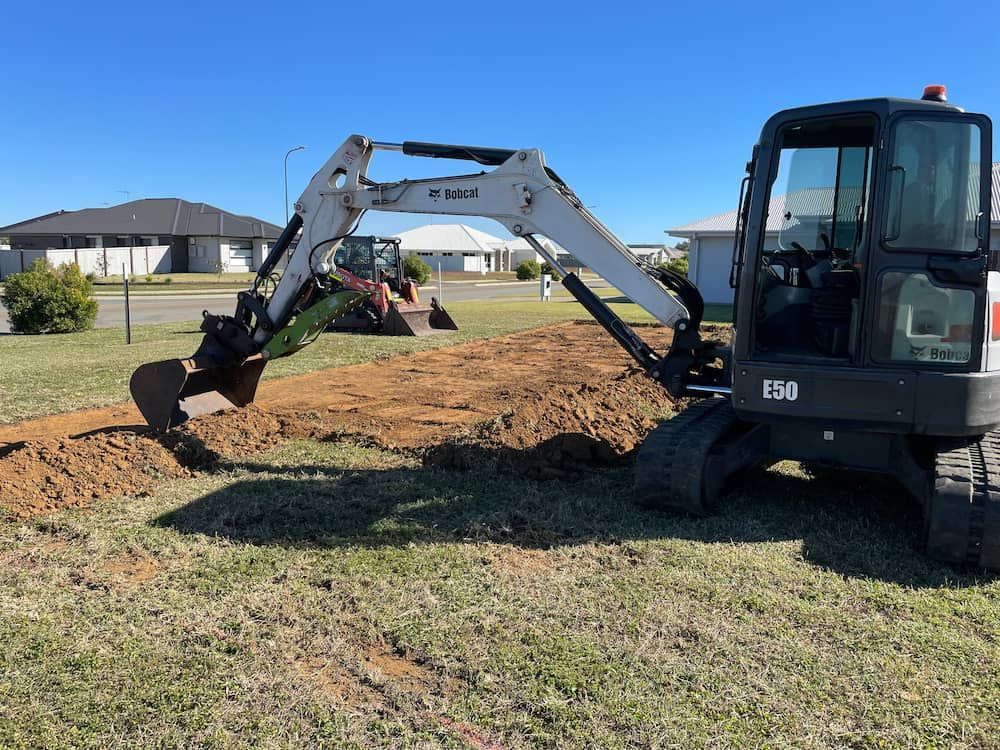 A Bobcat Excavator Is Digging A Hole In A Grassy Field — Upgrade Earthworks In South Kolan, QLD