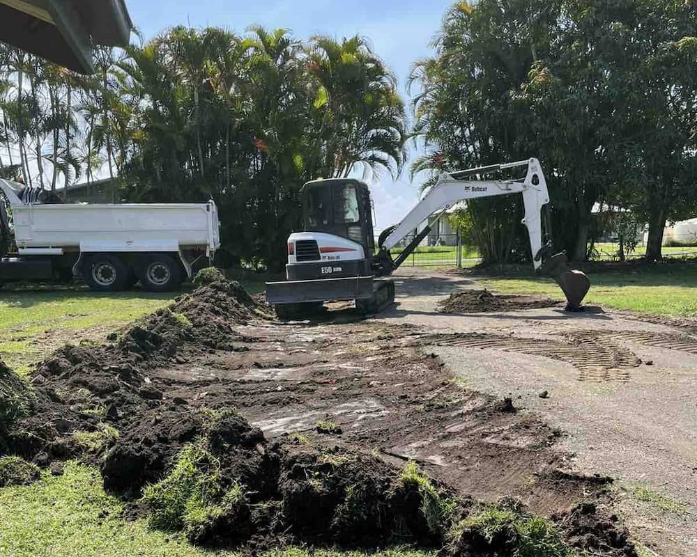 A Small Excavator Is Digging A Hole In A Driveway Next To A Dump Truck — Upgrade Earthworks In South Kolan, QLD