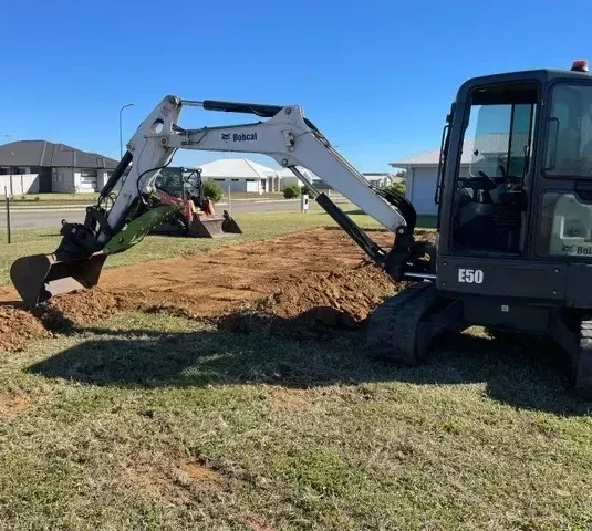 A Bobcat Excavator is Digging a Hole in the Ground — Upgrade Earthworks In South Kolan, QLD
