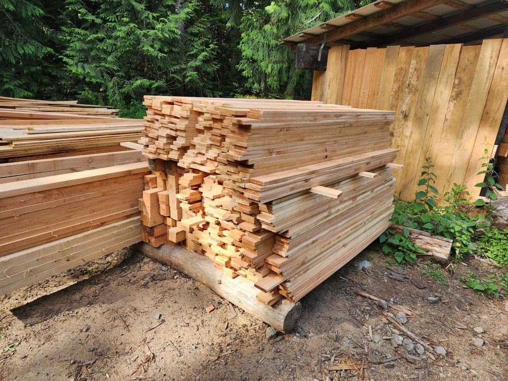 A pile of wood is sitting on the ground in front of a wooden shed.