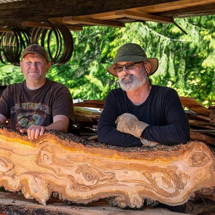 Two men are sitting next to a large piece of wood.