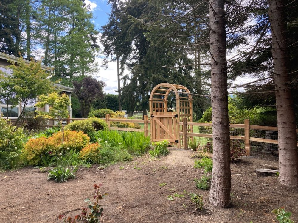 There is a wooden gate in the middle of a garden surrounded by trees.