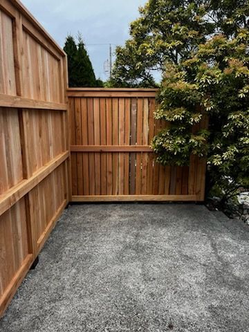 A wooden fence is sitting on top of a gravel driveway next to a tree.