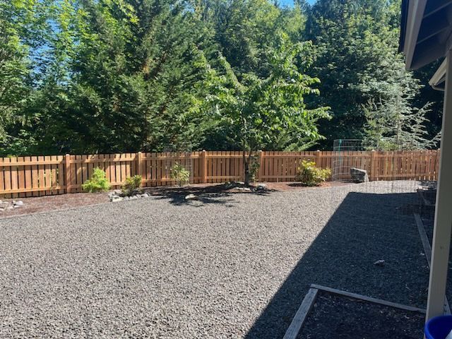 A gravel yard with a wooden fence and trees in the background