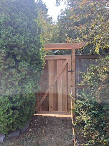 A wooden gate is surrounded by trees and a fence.