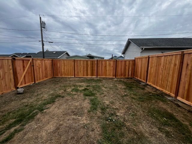 A wooden fence in a backyard with a house in the background.