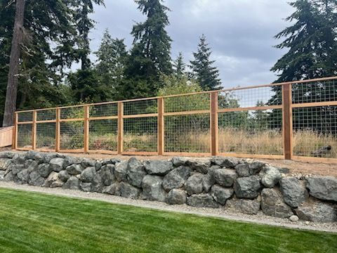 A wooden fence surrounds a rock wall in a backyard.