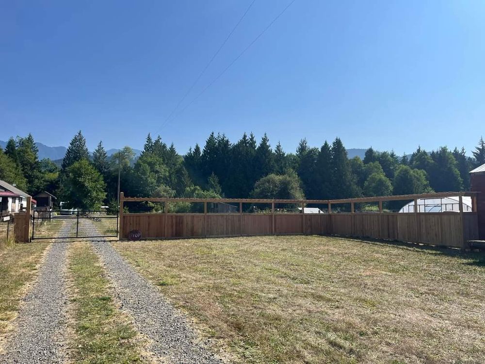 A wooden fence surrounds a grassy field with trees in the background.