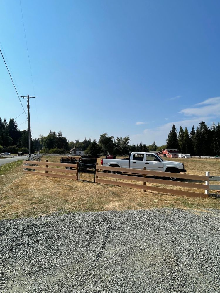 A white truck is parked in a gravel lot next to a wooden fence.