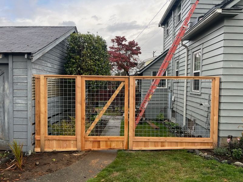 A wooden gate is in front of a gray house.