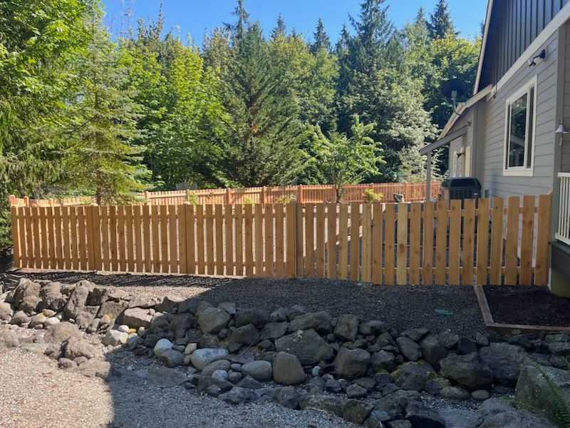 A wooden fence surrounds a rocky area in front of a house.