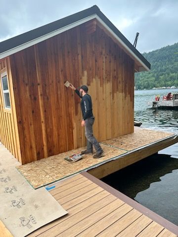 A man is painting a wooden building on a dock.