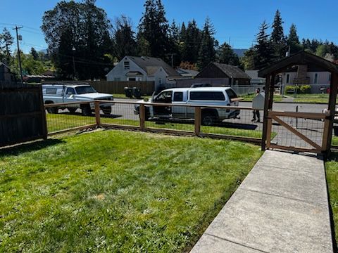 A white truck is parked in a grassy yard next to a wooden fence.