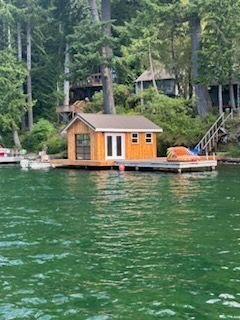 A small house is sitting on a dock in the middle of a lake.