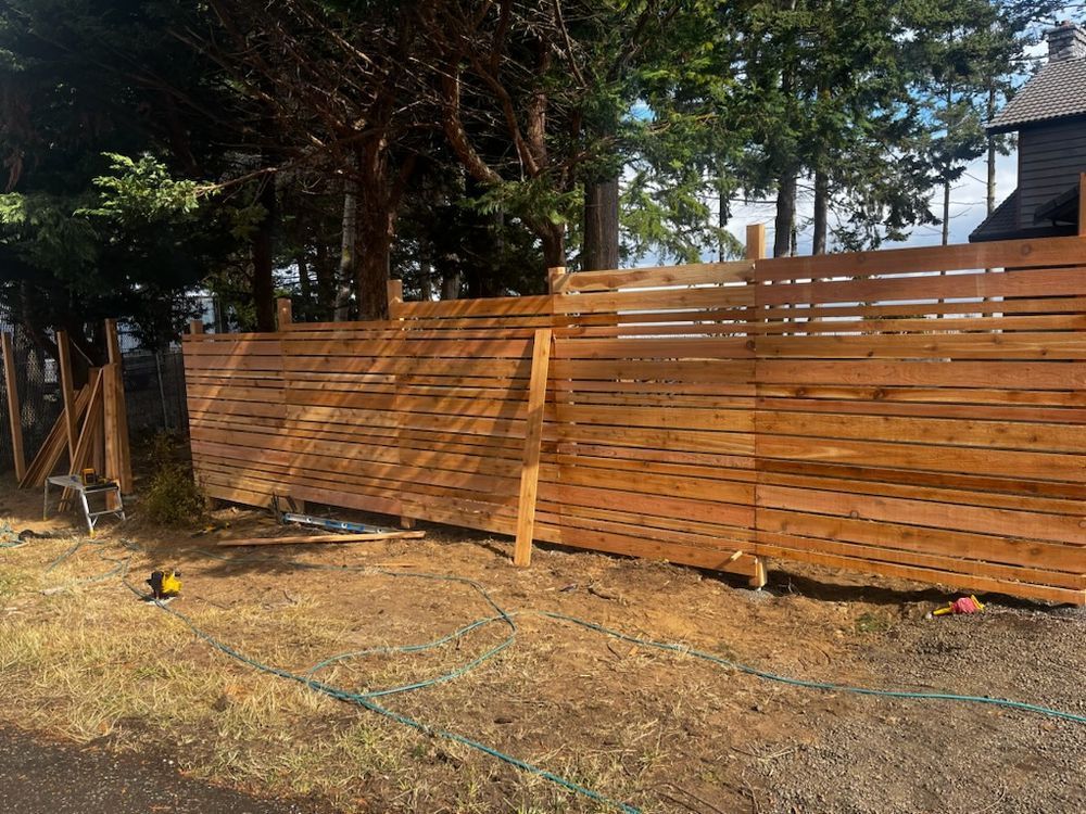 A wooden fence is being built in a yard with trees in the background.