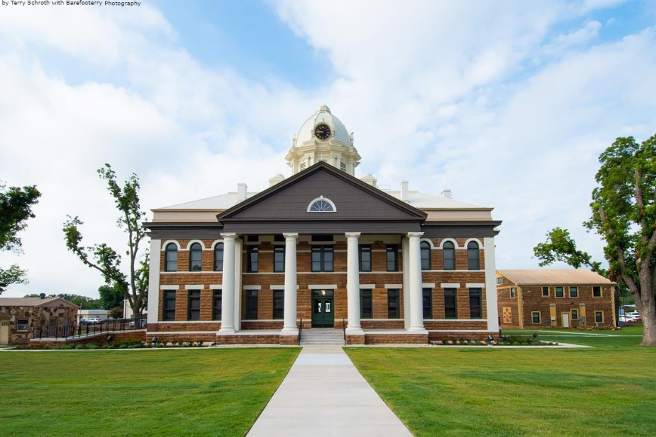Brown and white courthouse with large columns, topped with a golden dome, set on a grassy lawn.