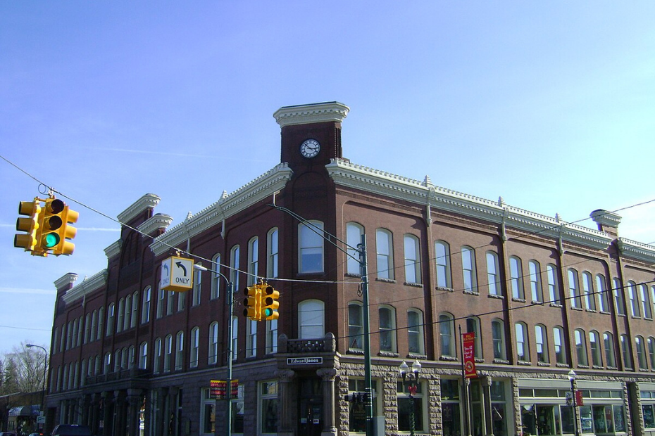 Brick building with clock tower on corner, traffic lights, blue sky.
