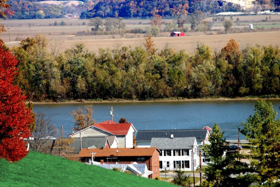 Riverfront town with colorful trees and a red barn in the distance.