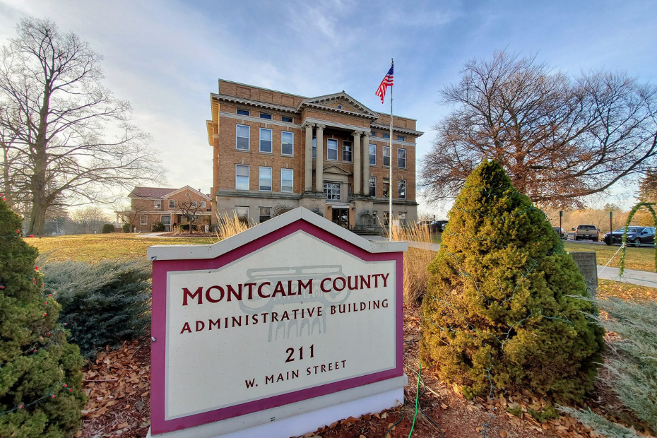 Montcalm County Administrative Building, brick building with sign at 211 W. Main Street, under a blue sky with trees.