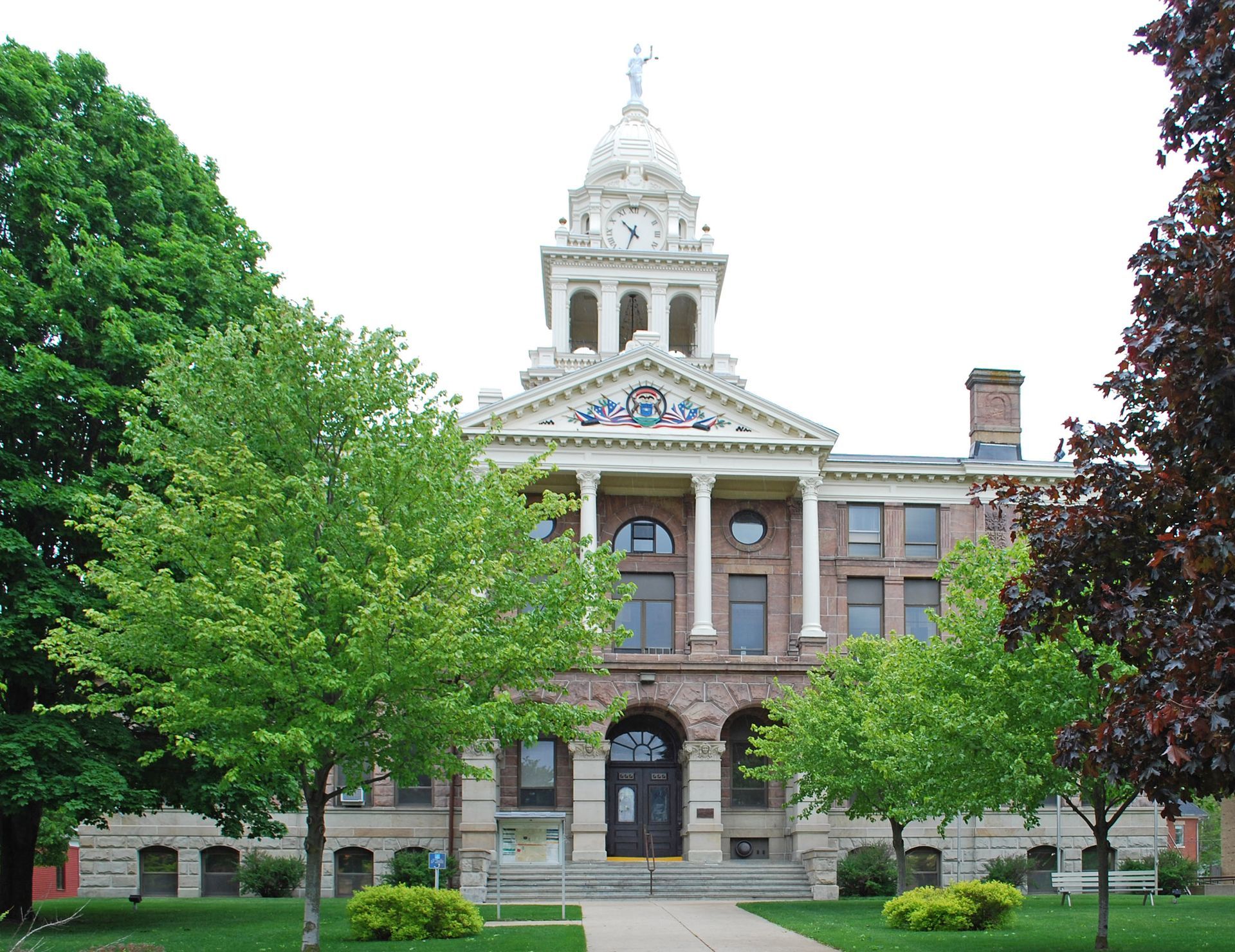 County courthouse with clock tower and columns, trees in front, green lawn.