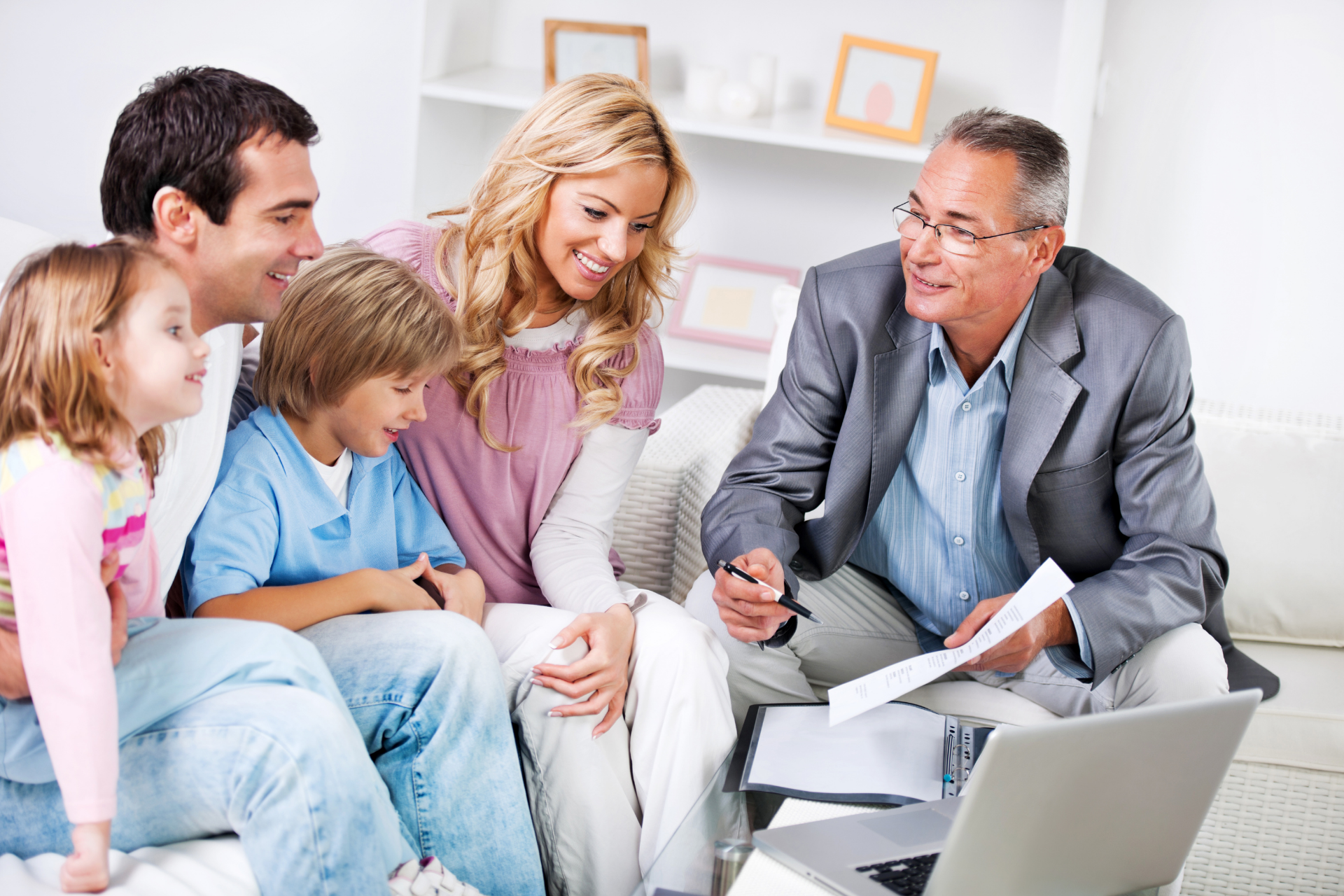 Family with two children consults with a financial advisor, discussing documents with a laptop present.