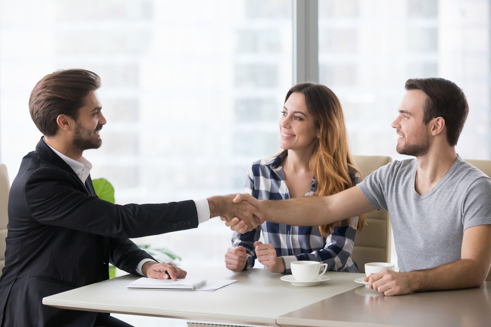 Man in suit shaking hands with a man at a table, woman smiling next to them.