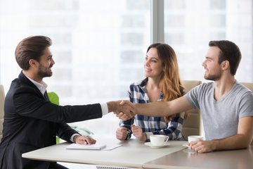 Man in suit shaking hands with a man at a table, woman smiling next to them.