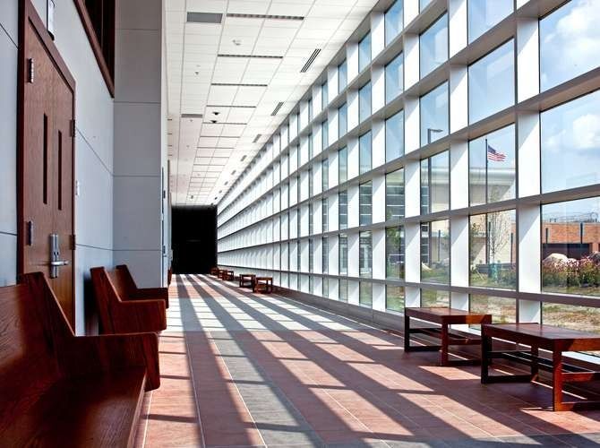 Hallway with floor-to-ceiling windows on the right, wooden benches on the left. Shadows of window frames on the floor.