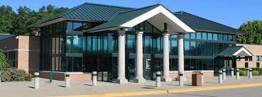 A modern building with a green roof, large windows, and three white pillars at the entrance.