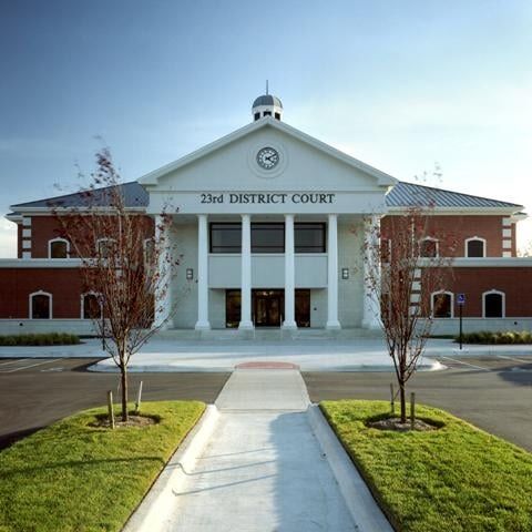 23rd District Court building with white columns, clock tower, and red brick exterior. Paved walkway and landscaping.