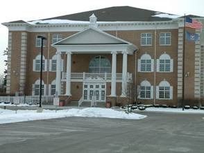 Two-story brick building with white columns and a small portico; snowy ground, American flag.