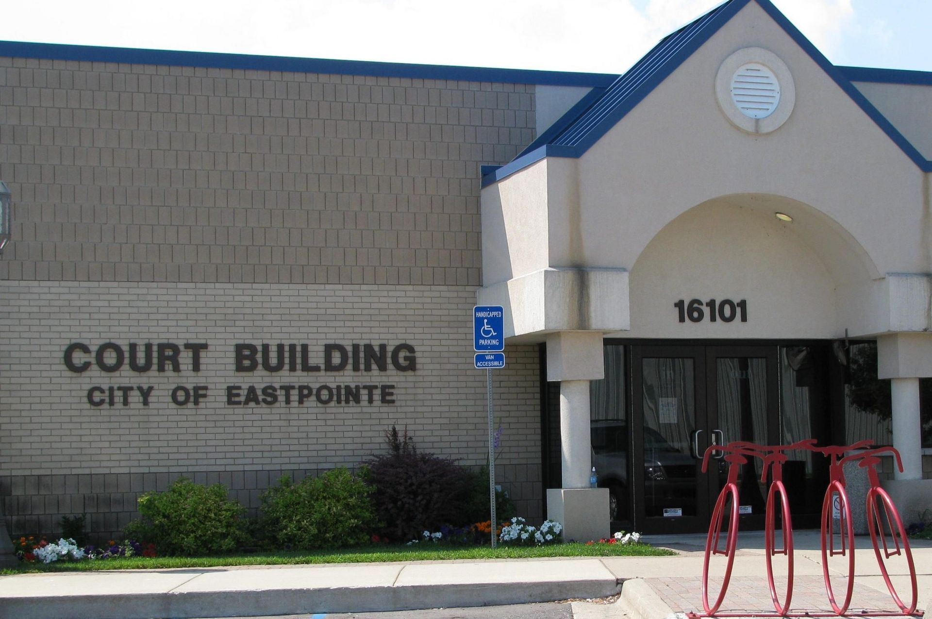 Court Building, City of Eastpointe. Beige brick building with blue roof over entrance, bicycle rack, and accessible parking sign.