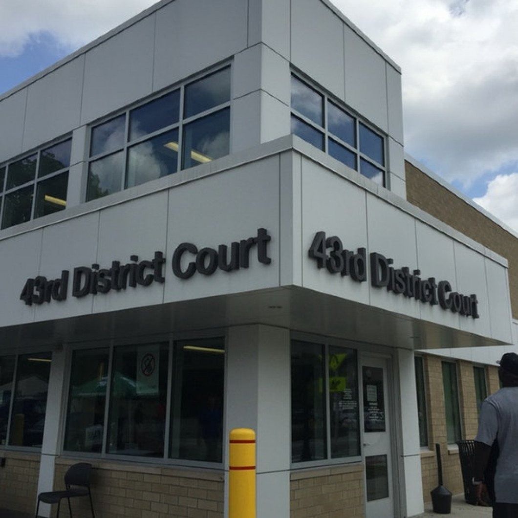 Exterior of the 43rd District Court building with large black lettering. Person enters the building on right.