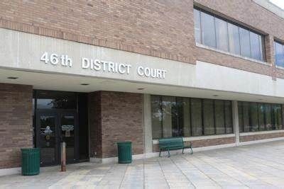 46th District Court building with brick facade and glass windows. Entrance features a door and two trash cans.