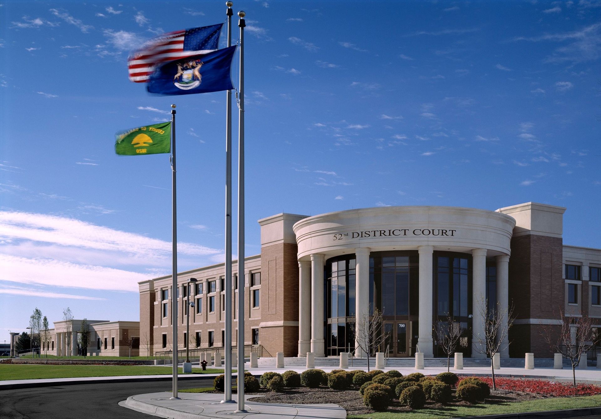 Court building with American, Michigan, and a yellow flags flying against a blue sky.