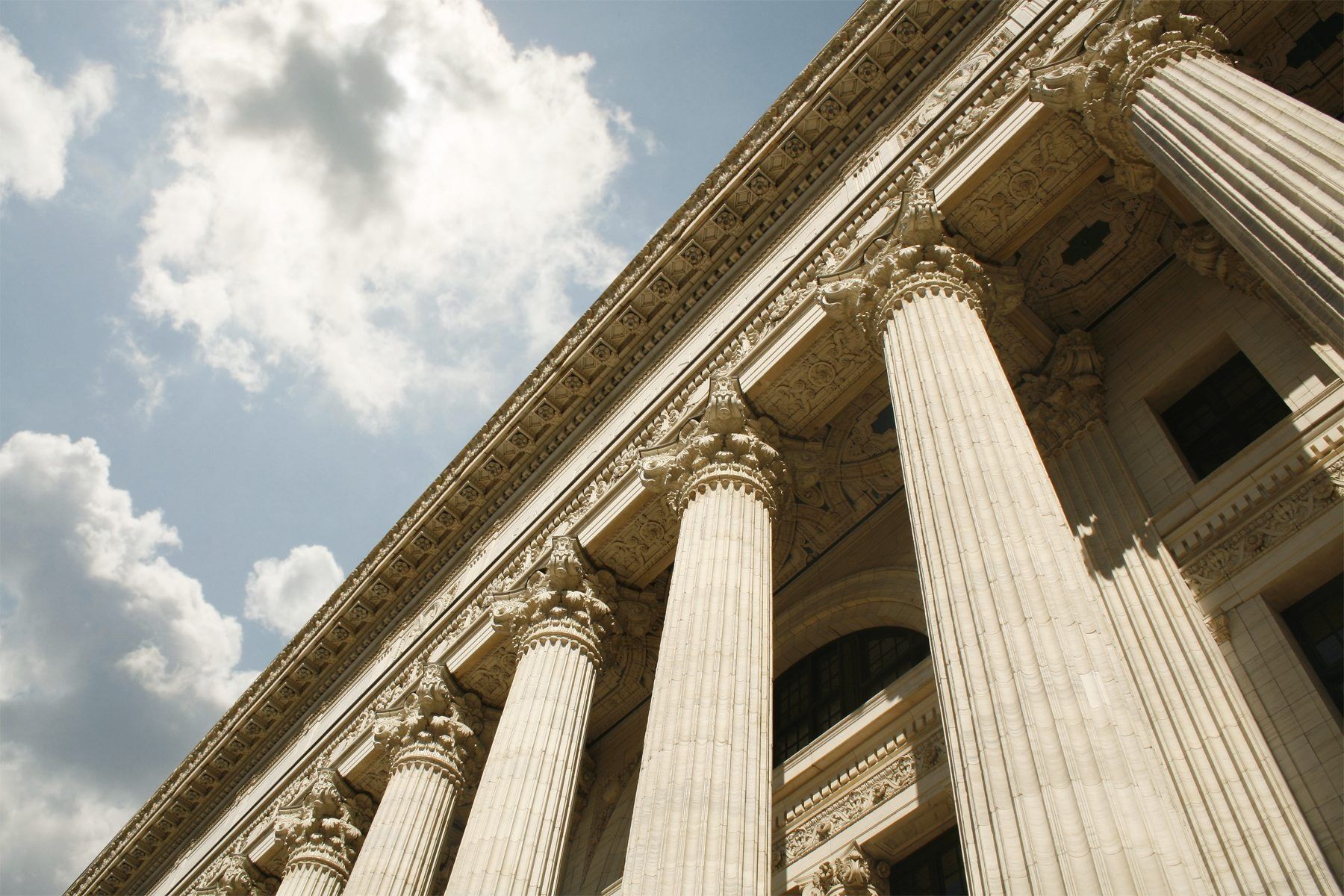 Beige building with tall columns against a partly cloudy blue sky.