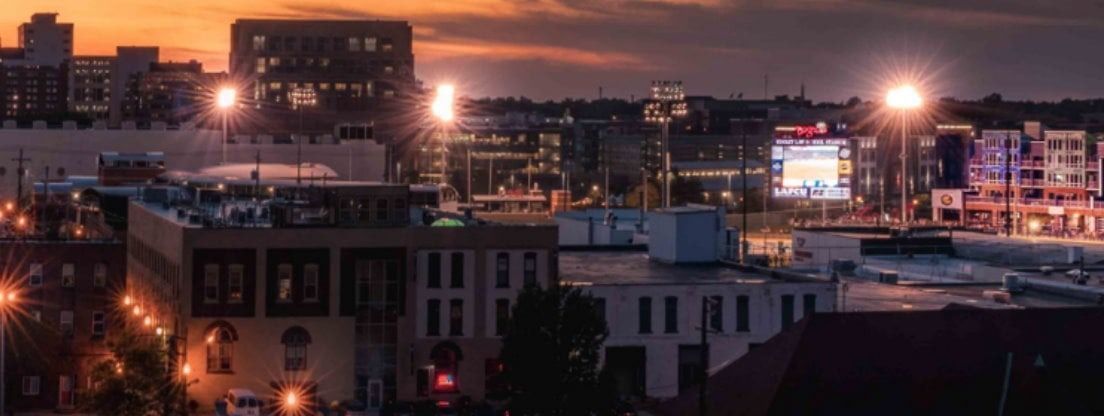 City skyline at dusk, buildings and streetlights, illuminated under a colorful sky.