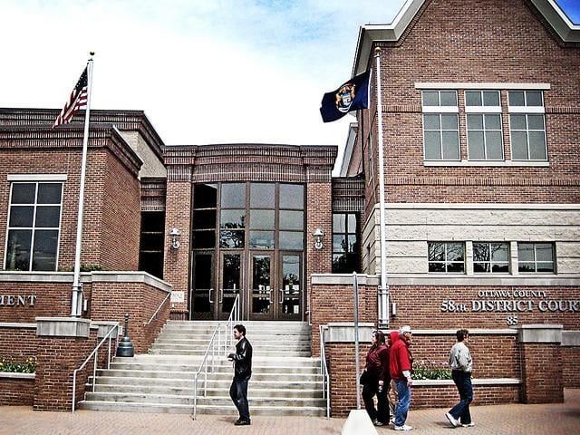 Brick courthouse with flags, glass doors, and people on steps.