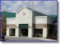 White and brick building with a green roof, labeled 