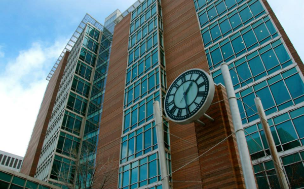 Tall brick and glass building with clock tower in the foreground.