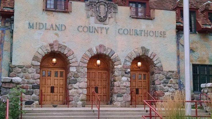 Midland County Courthouse, stone facade with three arched wooden doors. 
