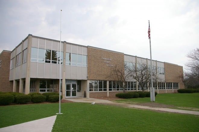 Two-story building with beige and brick exterior, windows, flagpole, and grassy lawn.