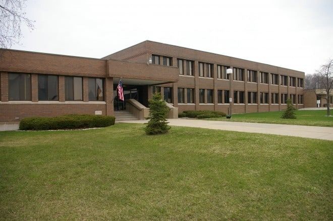 Brick building with rows of windows, small bushes, American flag, and green lawn.