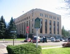 Large tan courthouse building with pillars, cars parked in front, sign in foreground.