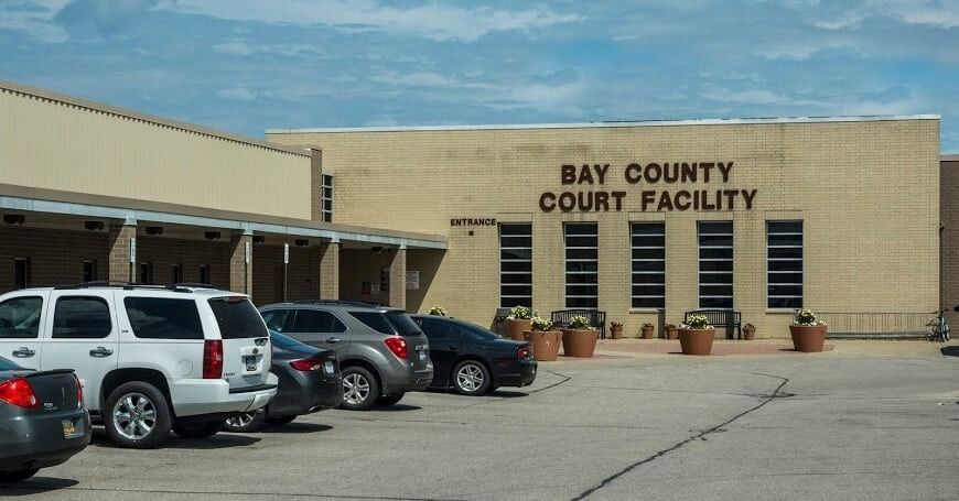 Bay County Court Facility exterior, cars parked in front of tan brick building with sign.