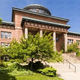Red brick building with columns, dome, and green trees on a sunny day.