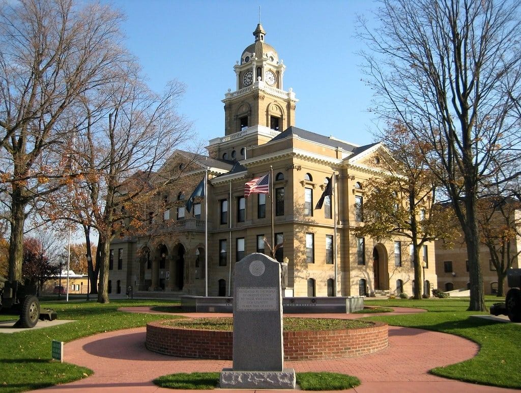 Courthouse with clock tower, brick walkway, and war memorial on a sunny day.