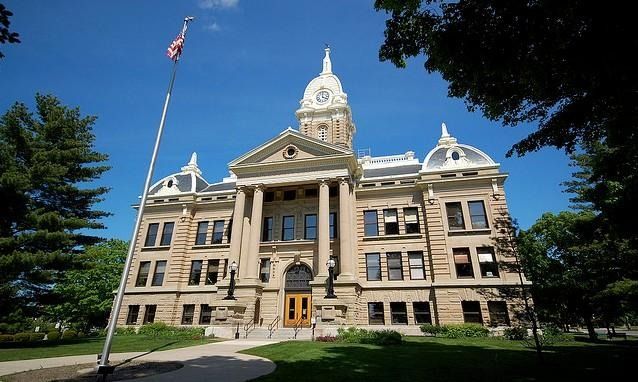Courthouse with columns, clock tower, and American flag on a sunny day.